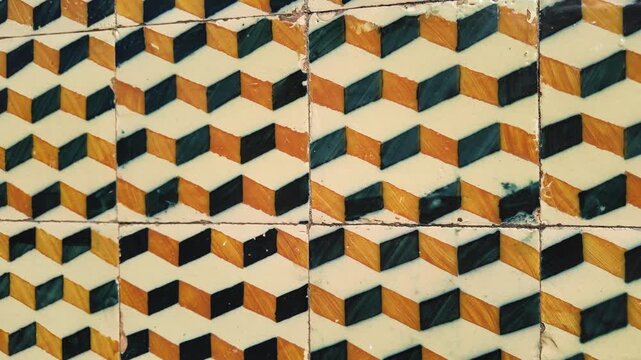 A close up of vintage ceramic tiles displaying a three dimensional geometric chevron design in black and orange. The weathered surface features visible brush strokes and aged glazing.
