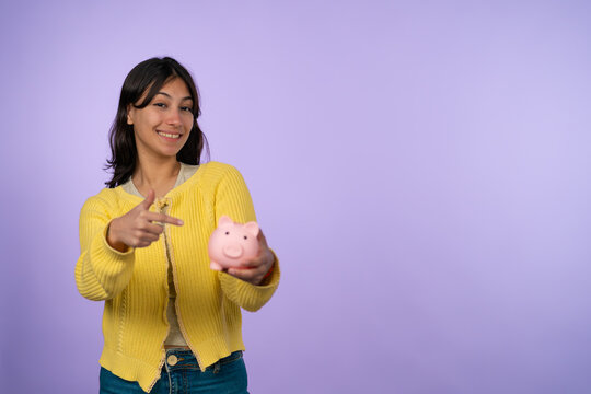 Young woman smiling while pointing at piggy bank
