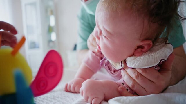 Baby being gently supported during tummy time while looking toward a colorful sensory toy