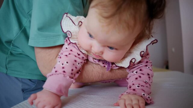 Baby being gently supported by an adult during a tummy time exercise on a padded treatment table