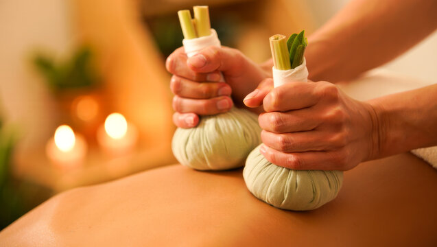 Spa therapist applying herbal compresses on a woman's back on a massage table, relaxation and wellness concept, thai massage, spa therapy, body treatment.