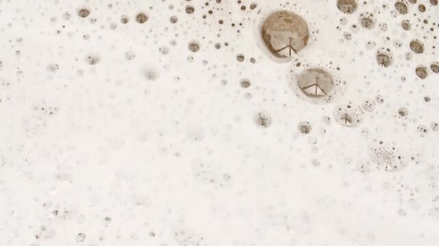 Waves of White Soapy Foam Flowing Down the Yellow Surface. Texture of Bubbles on abstract background. Soap sud macro structure. Bathtup Soap Foam. Natural White Shampoo Bubbles Motion. FullHD