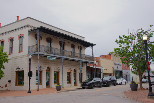 Historic Two-Story Building With Wrought-Iron Balcony on Small Town Commercial Street Edward Jones Sign. Editorial Use Only, Opelika, AL  USA, May 12, 2026. parked cars, trees, lamp posts and an overc