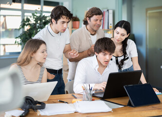 Fototapeta premium Team of employees gathers around single laptop, looking at screen and collaborating on common project or problem
