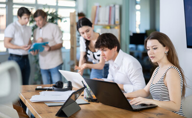 Fototapeta premium Young woman at her desk in modern office and working on laptop among group of colleagues