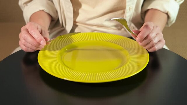 Person finishing a meal showing dining etiquette. Female hands placing a fork and knife on an empty yellow plate to signal the end of a meal, following proper dining etiquette