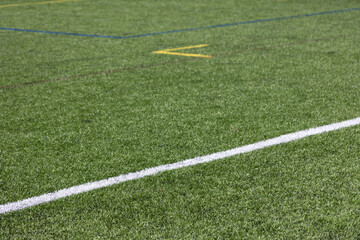 Obraz premium Close-up of an artificial turf sports field with marked lines crossing on synthetic grass. Outdoor sports surface suitable for football, soccer, training, and recreational activities.
