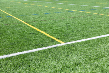 Obraz premium Close-up of an artificial turf sports field with marked lines crossing on synthetic grass. Outdoor sports surface suitable for football, soccer, training, and recreational activities.
