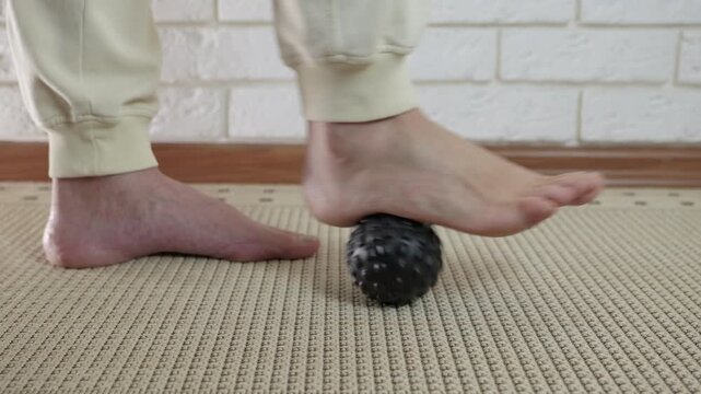 Plantar fasciitis foot massage with ball. Woman rolling his foot over a spiky massage ball for trigger point and self-massage therapy, helping to relieve pain from plantar fasciitis