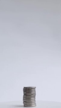 Male hand carefully picks up silver coins one by one and places each onto a growing vertical stack on white surface steadily building a tall coin column as savings concept