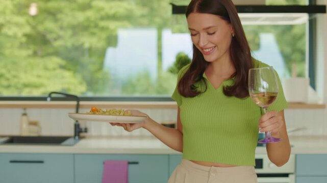 Happy young woman sitting at table with pasta and glass of wine, 4K slow motion