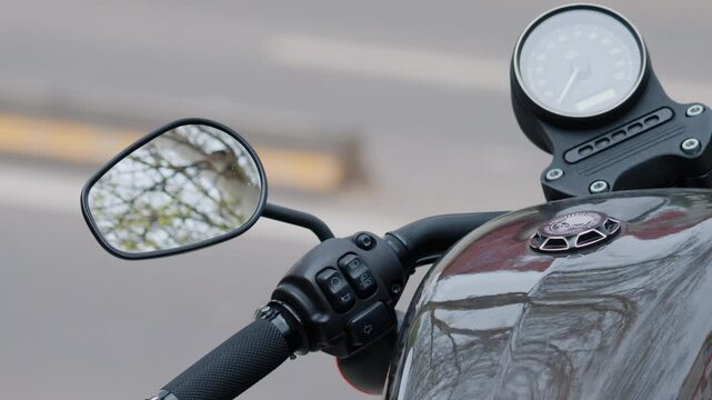 Close up view of a motorcycle mirror, handlebar controls, speedometer, and reflective fuel tank