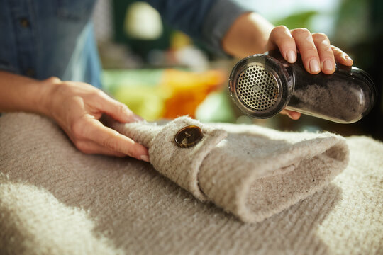 Close-up of hands using a fabric shaver on a winter coat highlighting the meticulous process of garment refreshing and pilling removal.