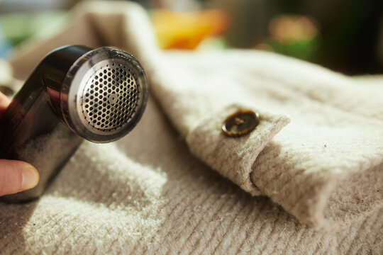 A handheld electric fabric shaver removes pilling from a beige textured wool sweater, illustrating essential garment maintenance and textile care for a lasting wardrobe.