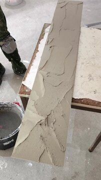 A man's hand applies cement adhesive to a long porcelain tile using a trowel.