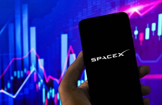 SpaceX logo on a smartphone screen with a stock market chart in the background.