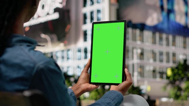 Vertical green screen tablet used by person to watch movies, sitting on bench in city park. African american young girl using chroma key device to relax, enjoying TV shows entertainment outside.