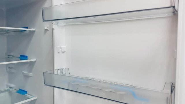 Empty white refrigerator interior glass shelves, closeup walkthrough of tempered glass door bins, bright studio lighting, pristine