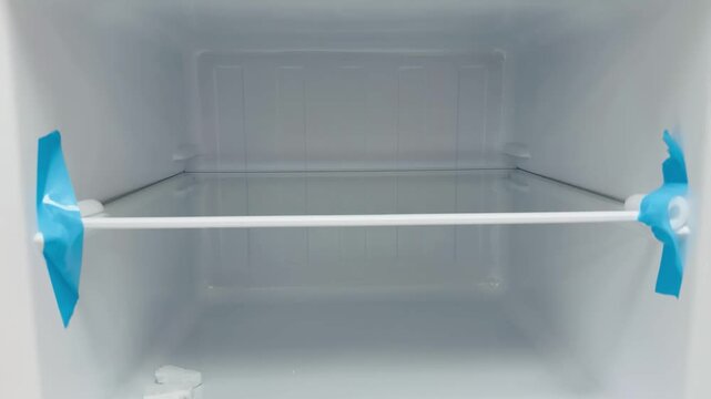 Empty freezer interior new refrigerator showing wire shelf with protective blue tape, open door, pristine white plastic walls