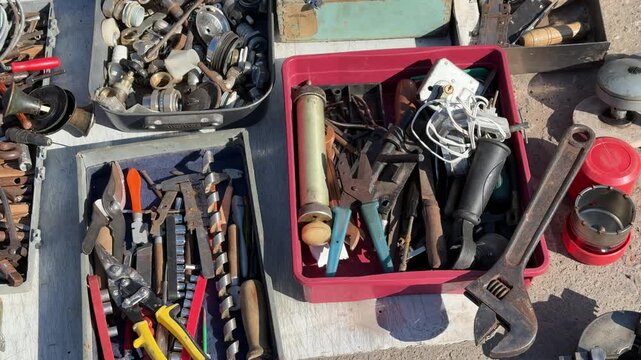 Assorted tools in boxes on asphalt selling secondhand household goods and tools for minor repairs sunlit flea market display