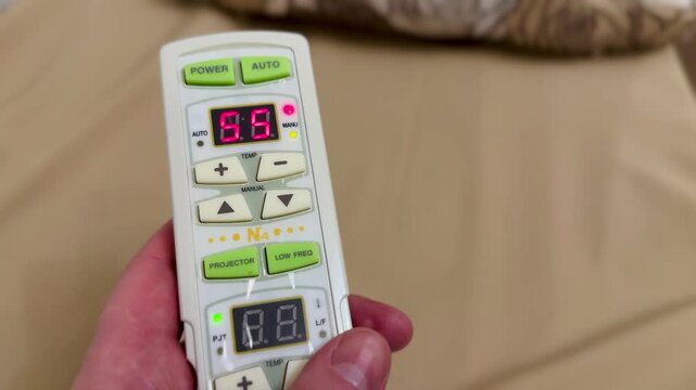 Close-up hand holding remote control adjusting heating temperature on massage bed, LED display changing digits, finger pressing