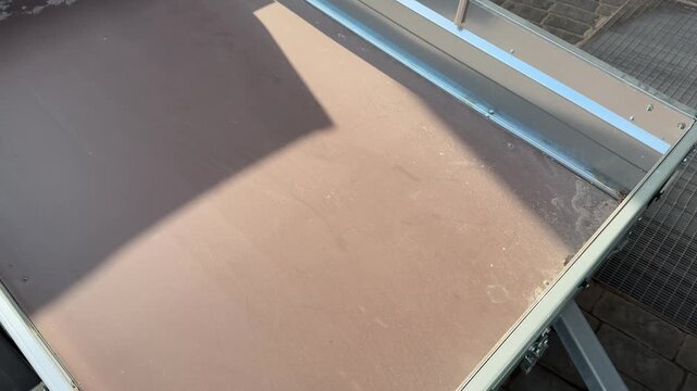 Top view empty trailer bed showing green metal frame and worn plywood floor with edge chips and small damage, sunlight casting