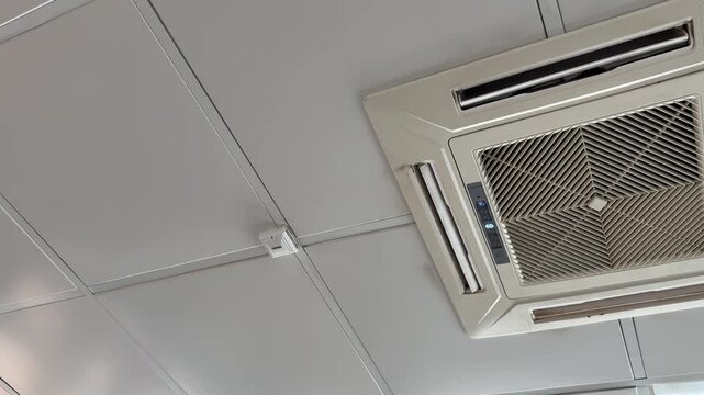 Ceiling cassette air conditioner unit mounted in suspended office ceiling grid, white grille and vents, closeup inspection