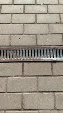 Patterned metal grate on paving stones, close-up view of linear drainage channel embedded in concrete pavers, rusted slats