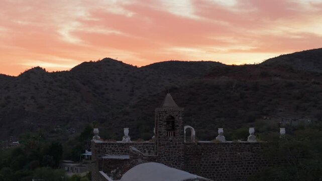 Aerial views show Mission Church Santa Rosalia in Mulege Baja California with palm trees, mountains, and the Sea of Cortez at sunset.