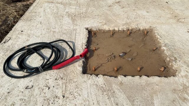 Ground hole with bolts and cable installer preparing concrete foundation for vertical billboard pole, coiled power cable