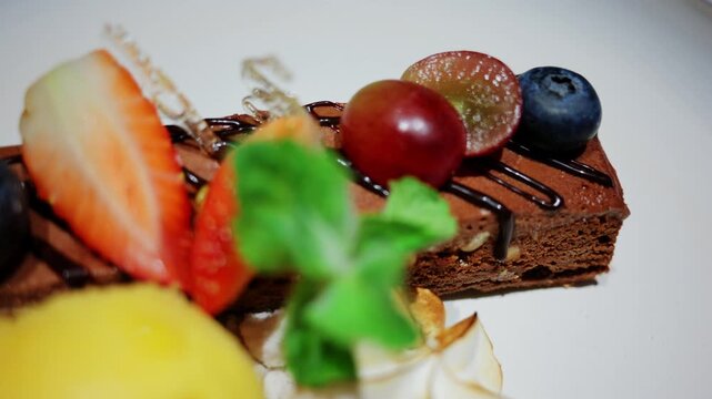 Close up of an elegant dessert served at a restaurant, featuring berries, cream, mint, chocolate, and a scoop of yellow sorbet