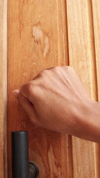 Close-up of a man's hand knocking on a modern door panel with a silver handle.