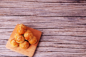 Fototapeta premium Kue Nastar or Golden pastries rest on a wooden board. Warm tones highlight crisp, inviting textures. Rustic wood adds cozy, homey charm. Perfect for food blogs or cafe promotions. 