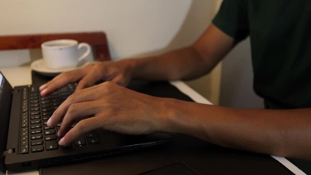 close-up video of hands typing on a laptop keyboard at a home workspace. 