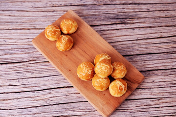 Fototapeta premium Kue Nastar or Golden pastries rest on a wooden board. Warm tones highlight crisp, inviting textures. Rustic wood adds cozy, homey charm. Perfect for food blogs or cafe promotions. 