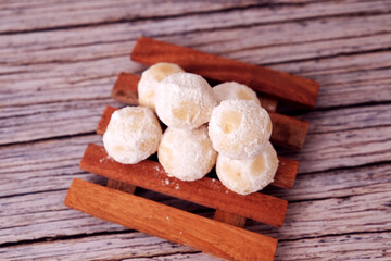 Fototapeta premium Kue Salju or Soft, round treats dusted with sugar sit on a wooden board. Wooden planks rest on a rustic tabletop. Shallow depth of field highlights texture and sweetness. Perfect for food blogs 
