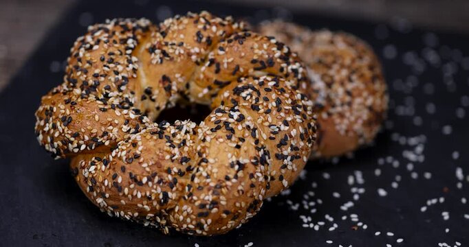 Golden-colored simite on black slate, this simite with black and light sesame seeds has a dense texture and is set against a dark stone background.