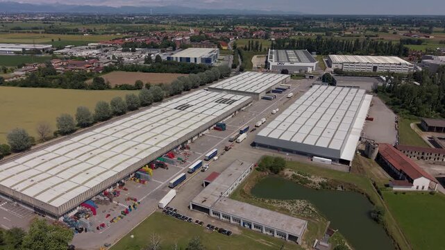 Industrial Landscape: An aerial view reveals a sprawling industrial complex with long, low-rise warehouses, rows of trucks, and a small pond, signifying economic activity and logistics.