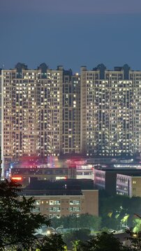 Vertical video, two high occupancy residential buildings with nearly all windows lit up at night.