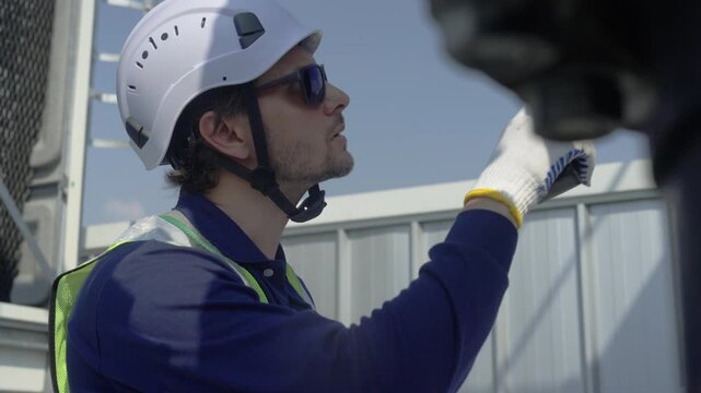 Engineer maintenance hvac cooling tower technician radio rooftop safety inspection with hard hat helmet glove, calm focused repair service and routine maintenance, inspects under blue sky daylight