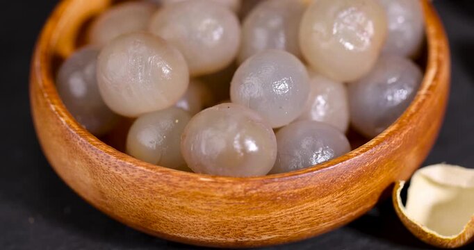 Juicy transparent longan in a bowl, peeled longan without a hard shell fills a wooden bowl on a black slate board in the frame.