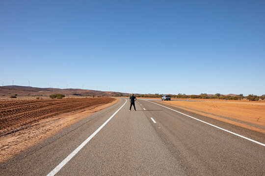 Lone traveler stands on a vast, empty highway stretching through the Australian outback
