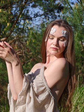 Mystical young woman with silver face art posing in sunlit forest