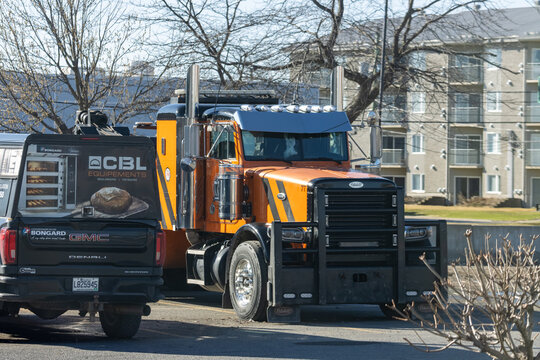 Quebec, Canada, 24 April 2026 : An orange Peterbilt semi-truck is parked next to a black GMC Denali pickup truck with a CBL Equipements advertisement.