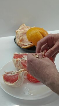 A detailed vertical close-up shows male hands carefully peeling the skin and white pith from a vibrant pink grapefruit, segmenting it for a nutritious and refreshing meal.