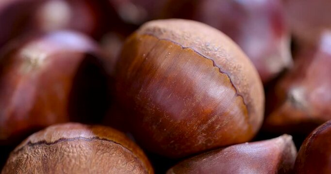 Whole chestnuts in a bowl, this chestnut product is ready for heat treatment and is located inside a vessel on a dark wood surface.