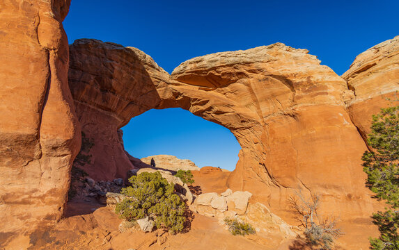 Sunlight illuminates a massive natural sandstone arch in a desert canyon.
