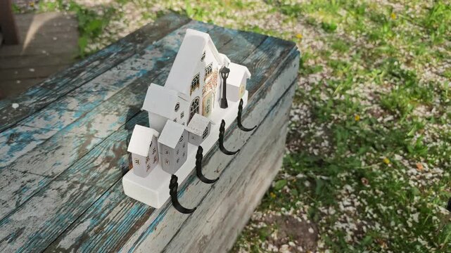 Detailed close-up footage of a unique handcrafted wooden key holder resembling a picturesque village with several small houses and a street light, positioned on a rustic blue wooden bench in a