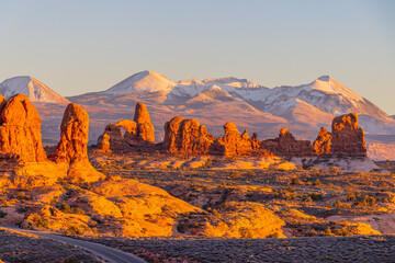 Sunlight illuminates red rock formations against snowy mountains. © Kit Leong