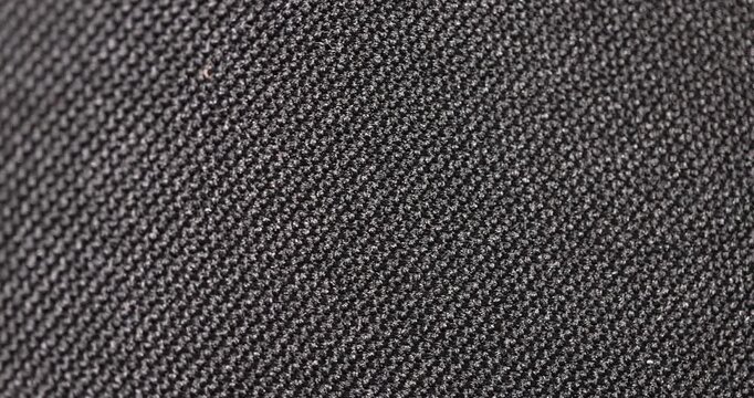 The fabric has a dense weave, a black synthetic fabric with a grainy surface and fine loops in side lighting with clear details and an organic texture in the macro.
